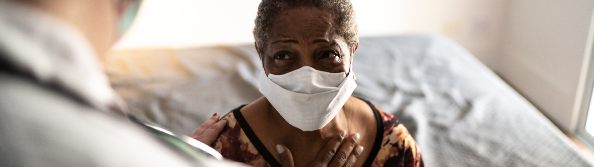 Patient speaks with doctor, with a hand on chest and wearing a mask.