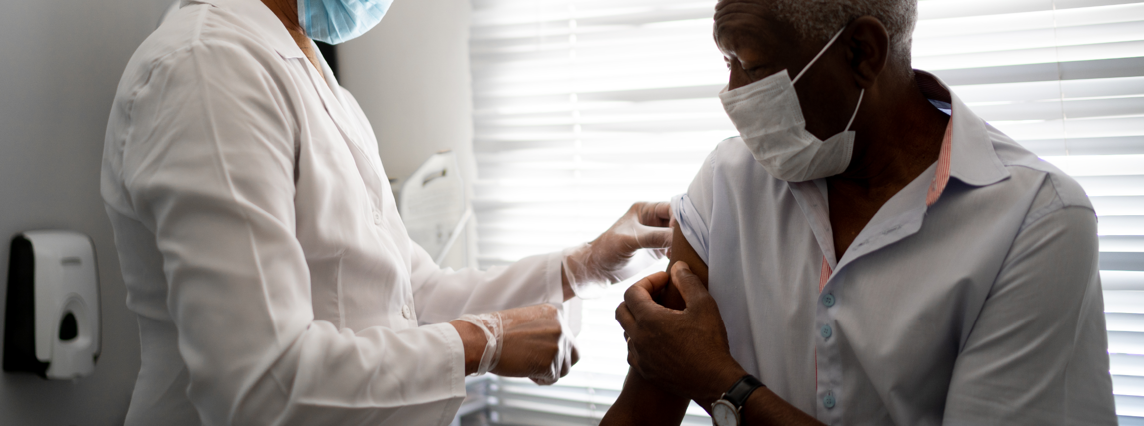 Medical professional administers vaccine to a patient, both wearing masks.